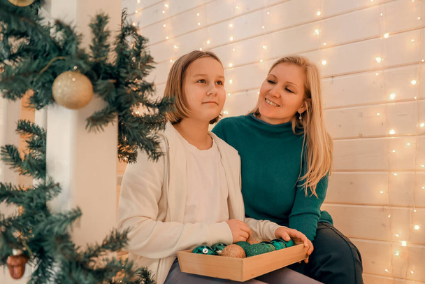 Happy mother and little daughter are decorating christmas tree at home. Family, winter holidays and people concept - Photo, Image