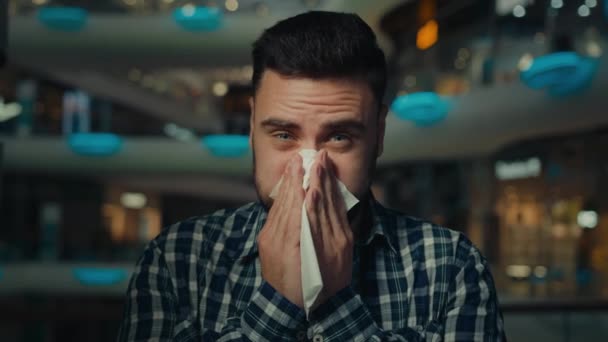 Homem doente árabe jovem homem alérgico no centro comercial sofrem de corrimento nasal gripe doença sazonal alergia cobrir boca espirro limpar nariz com guardanapo de papel tem sintomas virais infecção por coronavírus - Filmagem, Vídeo