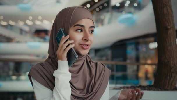 Piękna muzułmanka w hidżabie siedzi w miejscu publicznym rozmawiać telefon komórkowy w centrum handlowym kobieta millenium arabski dziewczyna zrelaksowany businesswoman dzwoniąc odległe do przyjaciela omówić rozmowę biznesową - Materiał filmowy, wideo