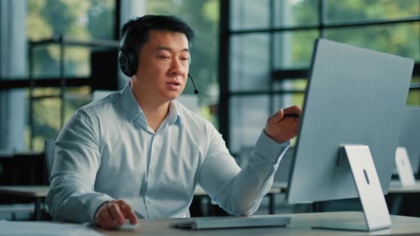 Китайский мужчина азиатский зрелый бизнесмен консультант офис-менеджер корейский человек в наушниках общаться онлайн с помощью компьютерных видео-звонок приложение принять участие в виртуальном брифинге объяснить бизнес-стратегию - Кадры, видео
