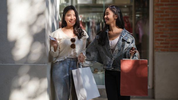 Şehirde alışveriş torbalarıyla dolaşan iki mutlu kız arkadaşın görüntüsü..  - Fotoğraf, Görsel