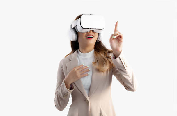 Asian woman in beige color jacket suit wearing vr goggles headset watching and finger pointing on white background. Metaverse and technology concept. - Foto, Imagem