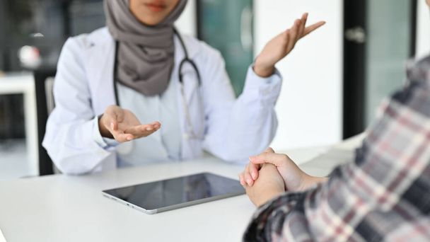 levágott kép, egy hivatásos ázsiai muszlim női orvos beszél egy beteggel az irodában, elmagyarázza az egészségügyi biztosítási ellátásokat, orvosi tanácsot és kezelési tervet ad. - Fotó, kép
