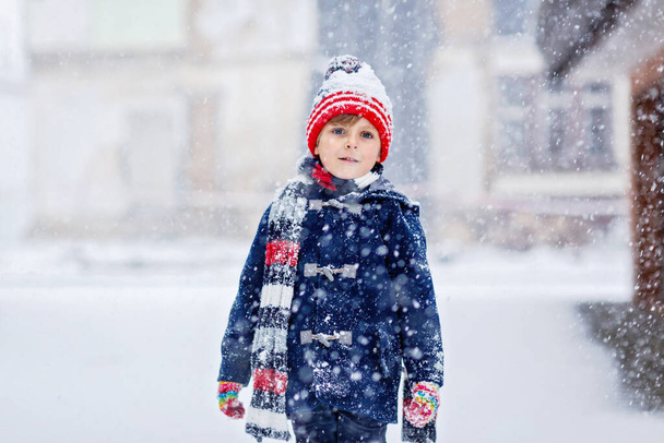 Preschool kid boy in colorful clothes playing outdoors during strong snowfall. Active leisure with children in winter on cold snowy days. Happy child having fun, playing with snow. Winter fashion - Photo, Image