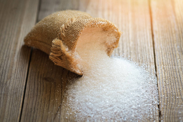 Suiker op zak en houten ondergrond, witte suiker voor voedsel en zoetigheden dessertsnoep hoop zoete suiker kristallijne korrels - Foto, afbeelding