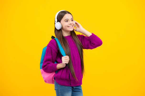 School teenager child girl in headphones with school backpack. Teenager student, isolated background. Learning music - Foto, afbeelding