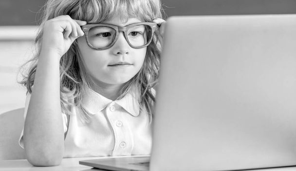 mały chłopiec w okularach studiować online w klasie szkolnej z komputerem, edukacja. - Zdjęcie, obraz