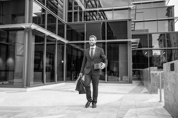 ευτυχισμένος επιτυχημένος γενειοφόρος επιχειρηματίας στο επίσημο κοστούμι περπάτημα με τσάντα αγορών παρουσιάζει εξωτερική πλήρες μήκος, closeout. - Φωτογραφία, εικόνα