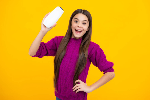 Excited face. Teen child girl with shampoo bottle or shower gel isolated on yellow background. Kids hair cosmetic product. Amazed expression, cheerful and glad - 写真・画像