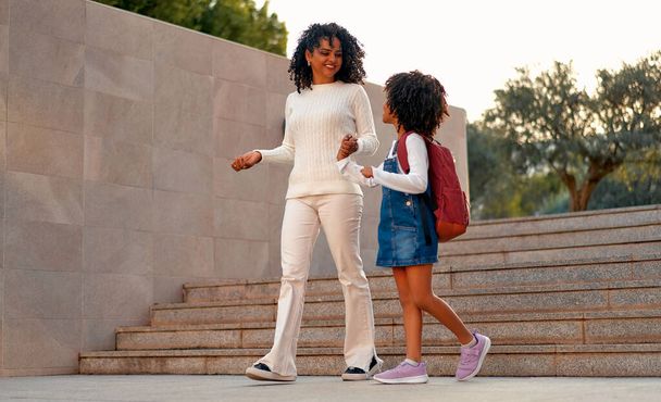 Glückliche afroamerikanische Mutter und Tochter Vorschulkind auf dem Weg zur Schule. Beginn des Unterrichts. Erster Herbsttag. Elternschaft oder Ausdruck von Liebe und Bindung. - Foto, Bild