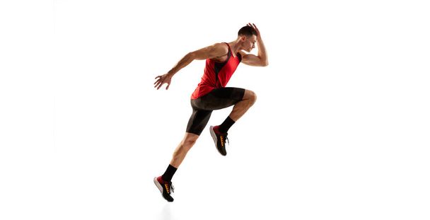 Jogger. Sportive man, muscular athlete, runner wearing bicycle shorts in motion and action isolated over white background. Energy, speed, sport and beauty concept. - Foto, imagen