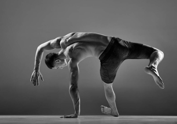 Black and white footage of male flexible muscular athlete showing animal flow sport elements isolated over gray background. Yoga, fitness, trendy sports, beauty. Grace and flexibility of human body - Foto, Imagem
