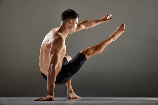 Portrait of male flexible muscular athlete showing animal flow sport elements isolated over gray background. Yoga, fitness, trendy sports, beauty of body. Grace and flexibility of human body - Fotoğraf, Görsel