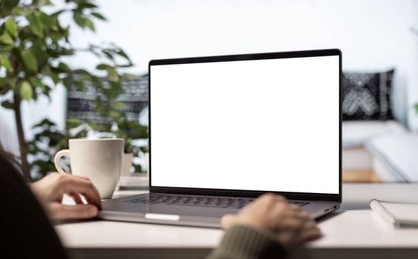 Современный ноутбук с чистым белым экраном для замены копии, женщина с помощью уютного домашнего света интерьер с чашкой парящего кофе - Фото, изображение