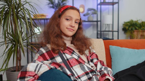 Close-up portrait of happy smiling young preteen student girl child kid 12 years old looking at camera on living room couch. Teenager children feel satisfied, dreaming resting, good news at home - Photo, Image