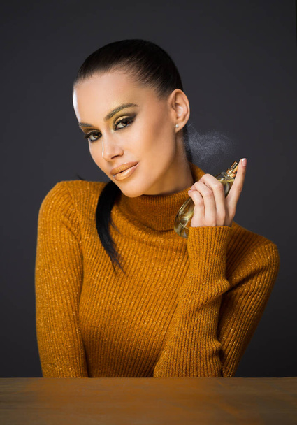 Beautiful young brunette model posing in golden luxury makeup using perfume. - Foto, immagini