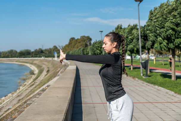 Young self loved teenage girl fitness exercises outdoor as morning routine for self-awareness of healthy life. Good posture woman stretching her muscles before workout training. - Foto, afbeelding