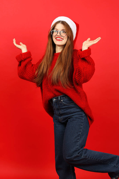 Confused and surprised young woman in santa hat on red background. New Year's fuss. - Foto, Imagen