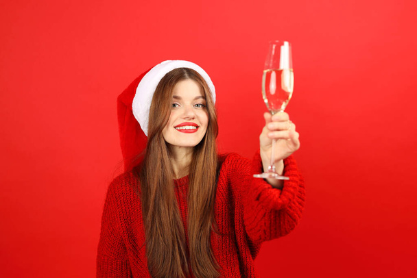 Christmas party, attractive young girl in santa hat and champagne glass on red background. - Фото, зображення