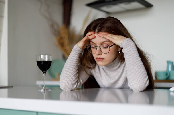 Sad and upset woman with a glass of wine at home. Headache, migraine. - Foto, imagen