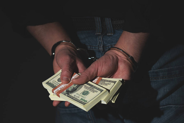 Corruption, illegal gratuities concept. Arrested man holding money in handcuffs. - Foto, Imagen