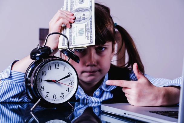 Business finance, banking and money concept. Young pretty business girl working in office. She holding money and pointing on alarn clock as if she wont to say: Have to be a friend of time - Photo, Image