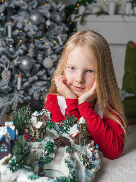Portrait of a little blonde girl who opens Christmas presents. Christmas tree and fireplace in the background. Close-up. Magical Christmas time. - Foto, Imagem