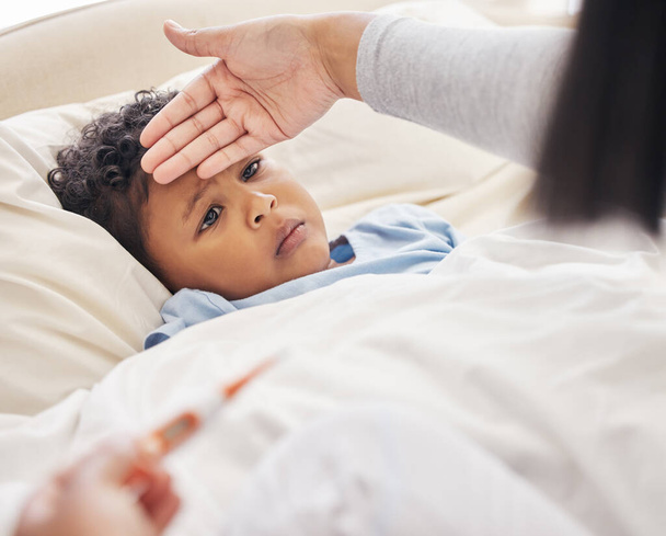 Sairas pieni poika makaa sängyssä, kun äiti mittaa kuumemittarin ja otsan tunteen. Kuumeesta kärsivää lasta hoitava äiti. - Valokuva, kuva