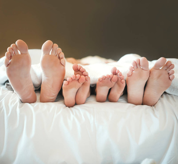 Gemütliche Familie, die zusammen im Bett liegt und es sich gemütlich macht, zusammen ein Nickerchen zu machen. Füße und Zehen von Eltern und ihren Kindern, die faul sind und sich tagsüber zu Hause auf einem Bett ausruhen. - Foto, Bild