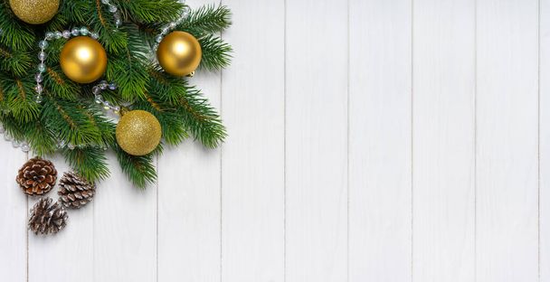 白い木製の背景にクラフト紙で金色のボールとモミのコーンで飾られたクリスマスツリーの枝。トップビュー、コピースペース付きフラットレイアウト、バナー、ヘッダー、新年の背景 - 写真・画像