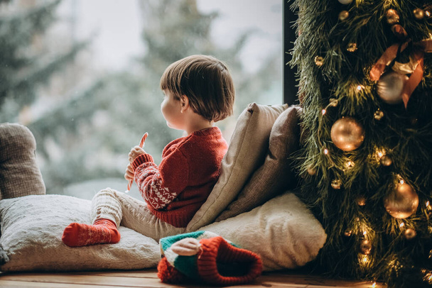 Das Kind sitzt am Fenster und wartet auf den Weihnachtsmann. Warten auf die Weihnachtsfeiertage. Glückliche Kindheit. Warten auf Feuerwehrleute. - Foto, Bild