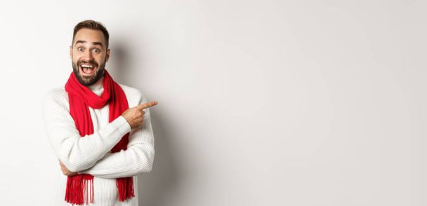 Natal feriados e conceito de celebração. comprador masculino barbudo animado mostrando seu logotipo, apontando o dedo para a direita em oferta promocional, de pé contra fundo branco. - Foto, Imagem