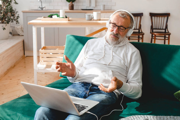 Elderly man making video call on laptop in room waving to screen and chatting with children - modern technologies communication internet - Foto, Imagen