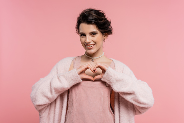 щаслива жінка в теплому і пухнастому кардигані, що показує знак серця з руками ізольовані на рожевому
 - Фото, зображення