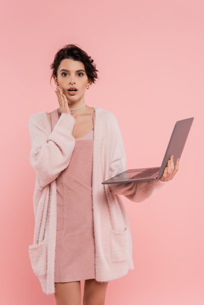 mulher preocupada com laptop tocando rosto e olhando para a câmera isolada em rosa - Foto, Imagem