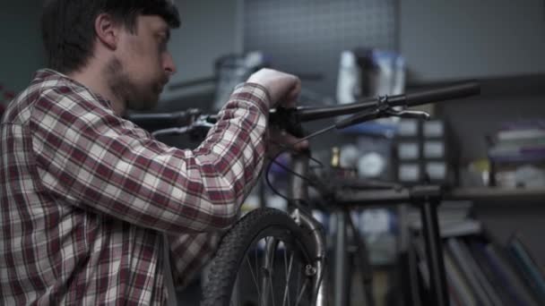 Bisiklet tamircisi bisiklet tamir ve ayarlama atölyesinde çalışıyor. Bisiklet teknisyeni bisiklet sapını ve gidonu özel aletle büküyor. Tamirci gidonu takmak için bir alet kullanıyor. Bisiklet servisi.  - Video, Çekim