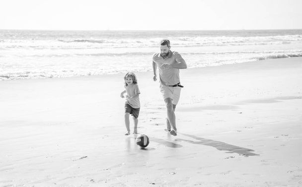 father and son play soccer or football on beach. daddy with kid boy on summer day. weekend family day. dad and child having fun outdoors. childhood and parenting. family holidays. sport activity. - Zdjęcie, obraz
