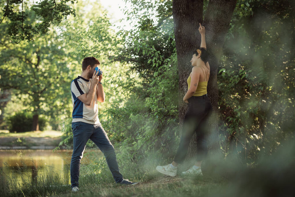 Oğlan, onlar ağacın yanındaki parkta dikilirken güzel kız arkadaşının fotoğrafını çekiyor. - Fotoğraf, Görsel