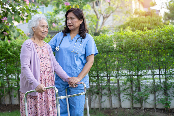 Médico ayuda y cuidado Asiático senior o anciana anciana mujer uso walker con fuerte salud mientras camina en parque en feliz vacaciones frescas. - Foto, imagen