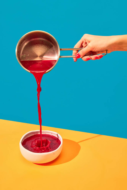 Woman pouring traditional Ukrainian dish, borscht into plate on yellow tablecloth over blue background. Red Beet soup. Popular dinner. Food pop art photography. Complementary colors. Copy space for ad - Φωτογραφία, εικόνα