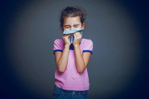 Kind niest vor grauem Hintergrund in Taschentuch - Foto, Bild