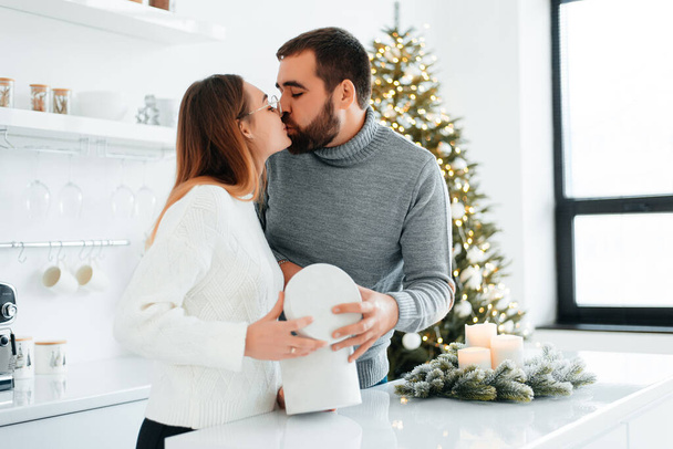 An attractive couple are opening their Christmas gifts near Christmas tree. - Foto, imagen