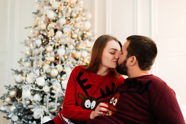 An attractive couple are opening their Christmas gifts near Christmas tree. - Photo, Image