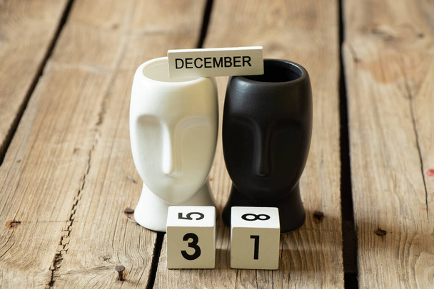 31 de dezembro dos cubos estão sobre a mesa perto das esculturas de rostos pretos e brancos, a data do ano novo e o calendário - Foto, Imagem