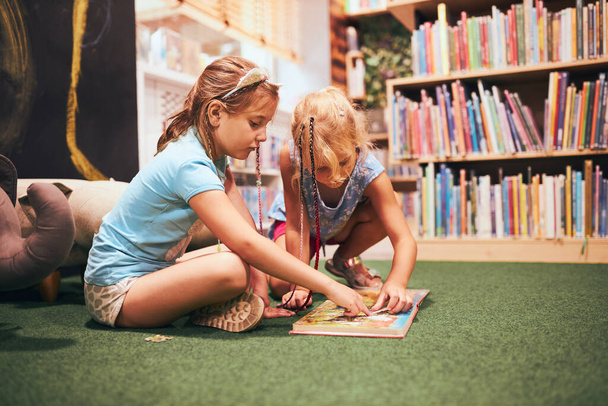 Two elementary schoolgirls solving puzzles and riddles in school library. Students learning from books. Pupils having fun in library. Back to school - Valokuva, kuva