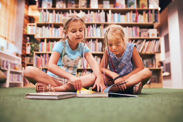 Two schoolgirls reading books in school library. Primary school students learning from books. Pupils doing homework. Children having fun with books in school club. Back to school - Fotografie, Obrázek