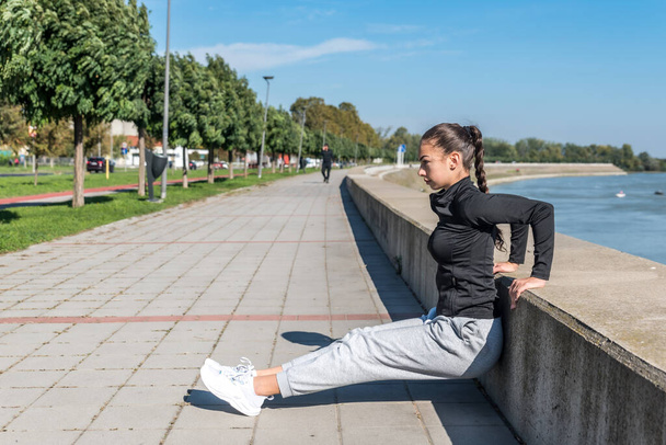 Young self loved teenage girl fitness exercises outdoor as morning routine for self-awareness of healthy life. Good posture woman stretching her muscles before workout training. - Фото, зображення