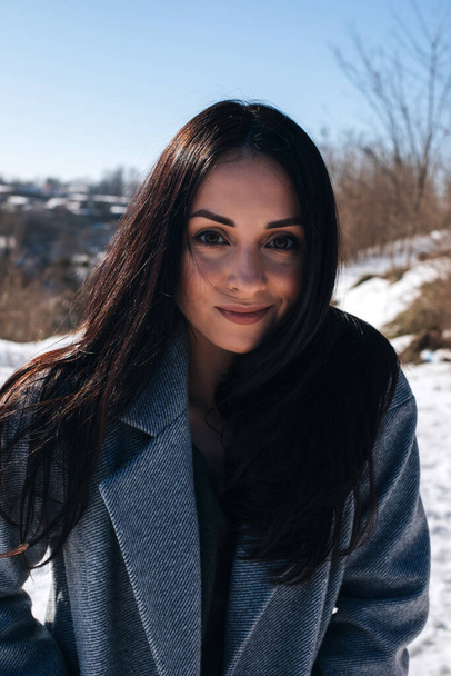 Retrato de una hermosa chica morena con ojos marrones en la calle en invierno nevado. Vista frontal - Foto, imagen