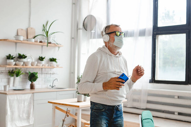 Senior man with medical mask on face using smartphone app for creating playlist music - Elderly male having fun with mobile phone technology - Photo, Image