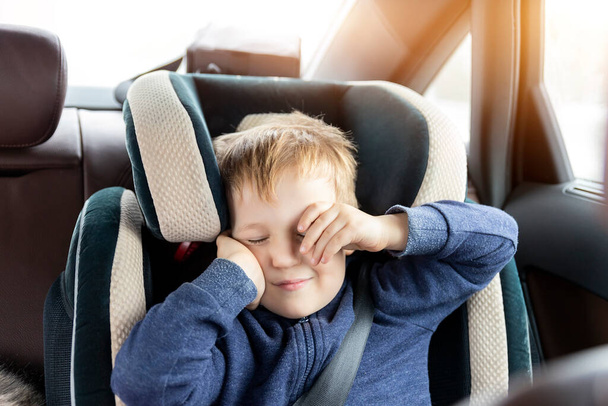 Cute caucasian toddler boy awaken and rub eyes in child safety seat in car during road trip. Adorable baby dreaming asleep comfortable chair during journey in vehicle. Children care safety on roads. - Photo, Image